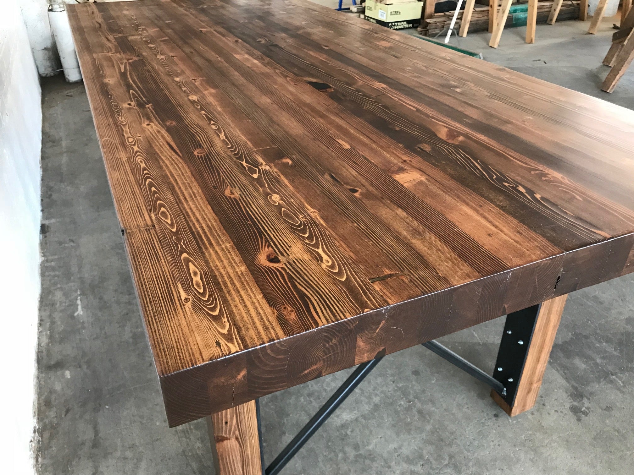 Dining table by Workshop Detroit - Made from reclaimed wood and steel shown in a walnut stain and sitting on a conrete floor