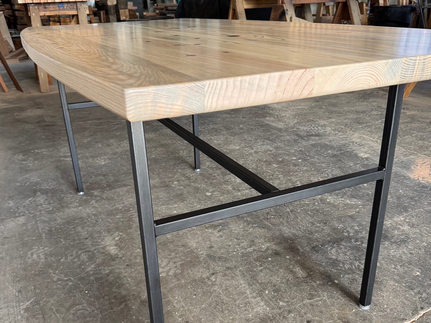 Close up of the Love For Humanity solid reclaimed wood dining table by Workshop Detroit. Shown in a workshop setting with a concrete floor.